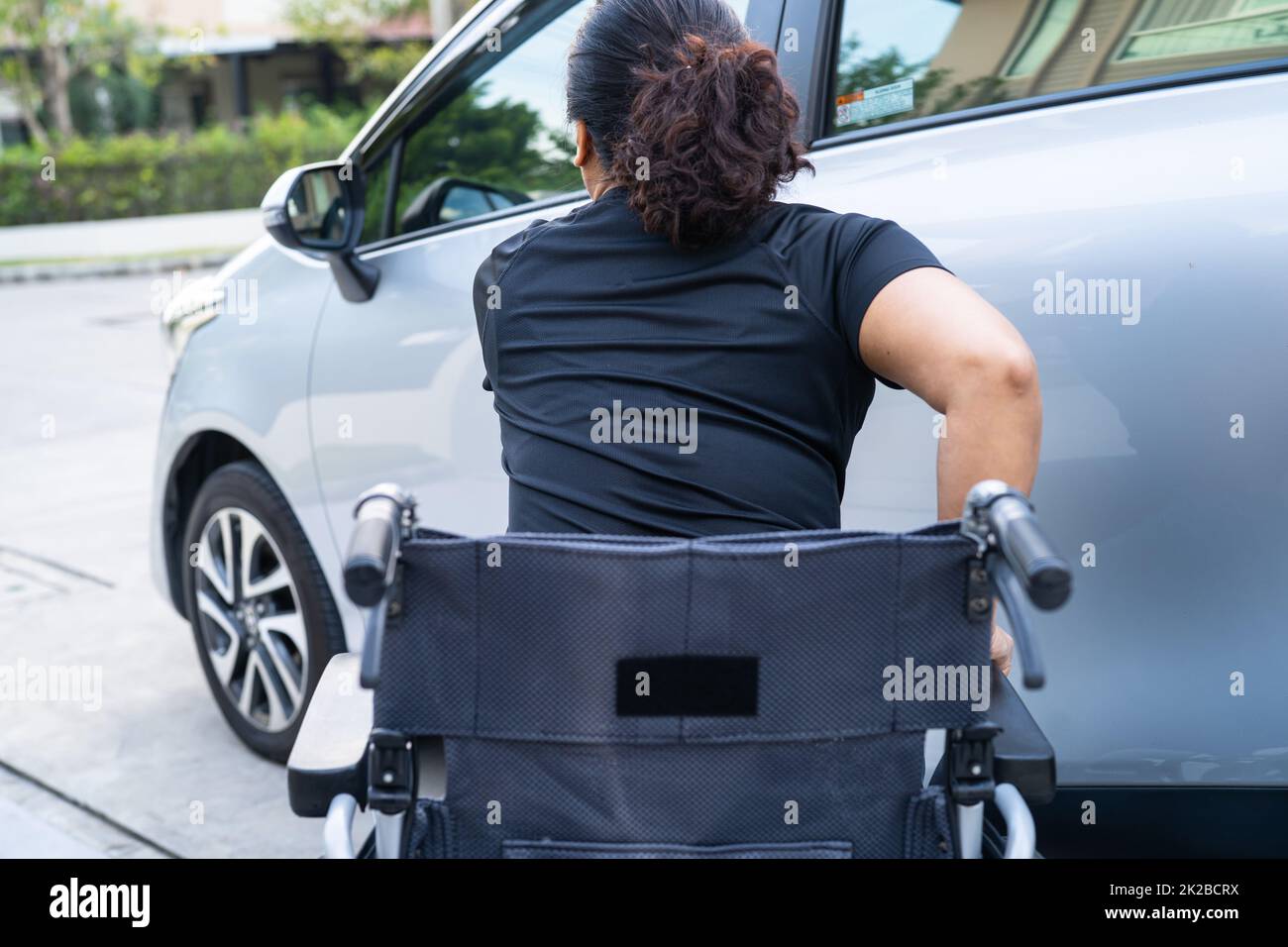Mujer con discapacidad asiática en silla de ruedas que se va a poner en su coche. Concepto de accesibilidad. Foto de stock