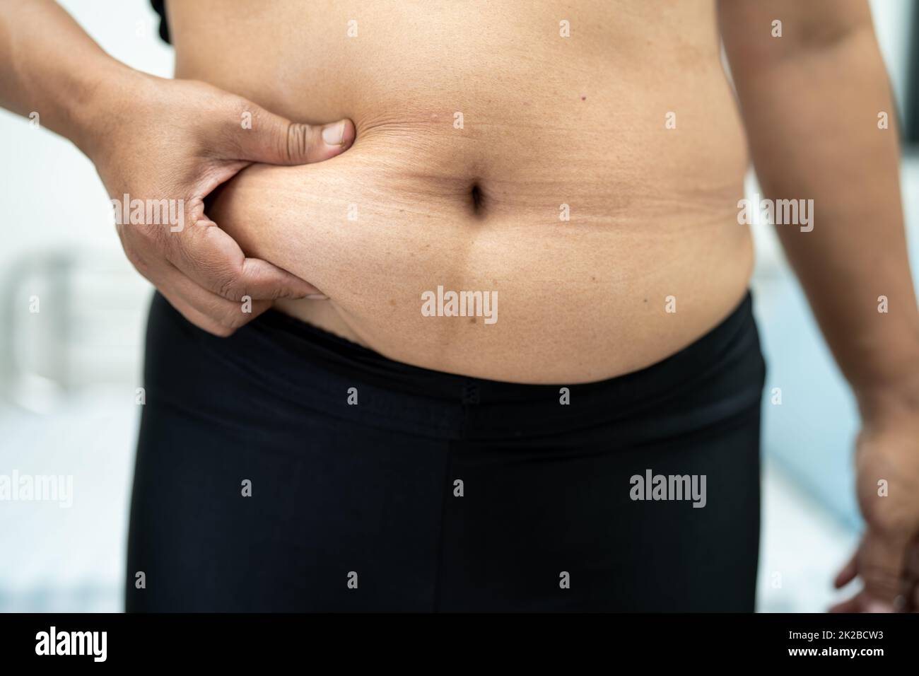 Mujer Asiática con sobrepeso muestran la grasa del vientre en la oficina. Foto de stock