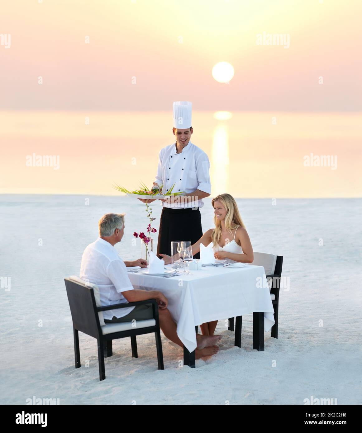 La cena romántica perfecta. Foto de una pareja adulta disfrutando de una cena romántica en la playa. Foto de stock
