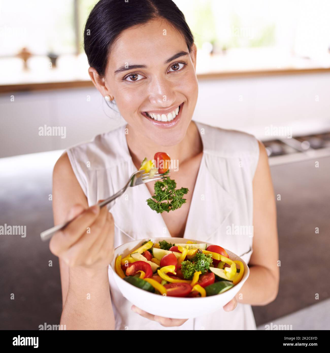 Deja que la comida sea tu medicina y la medicina sea tu comida. Mujer joven disfrutando de una ensalada mientras estaba de pie en su cocina. Foto de stock