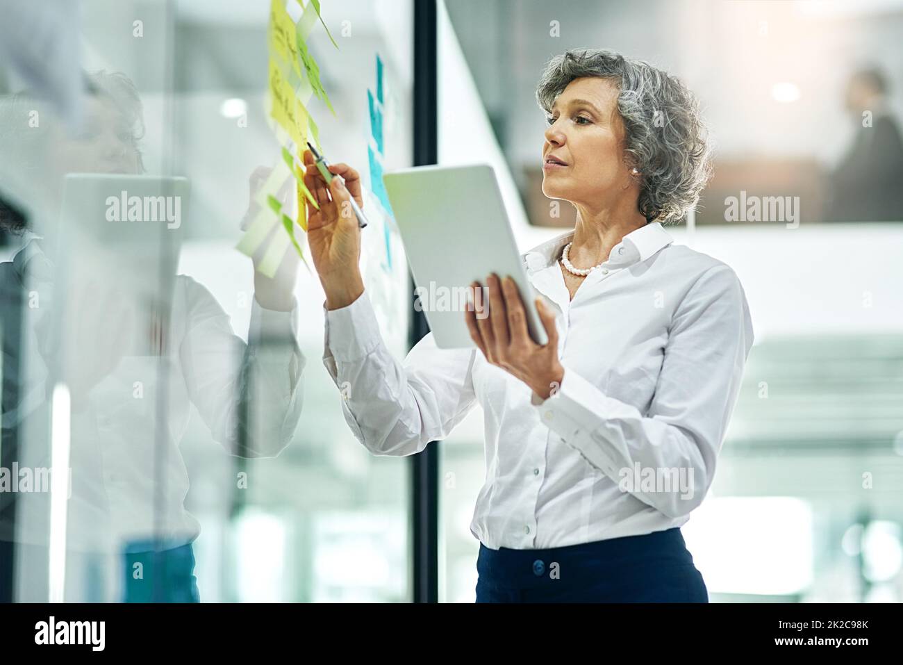 Trabajando hacia las metas de la carrera. Foto recortada de una empresaria  madura escribiendo notas en una pared de cristal en una oficina moderna  Fotografía de stock - Alamy