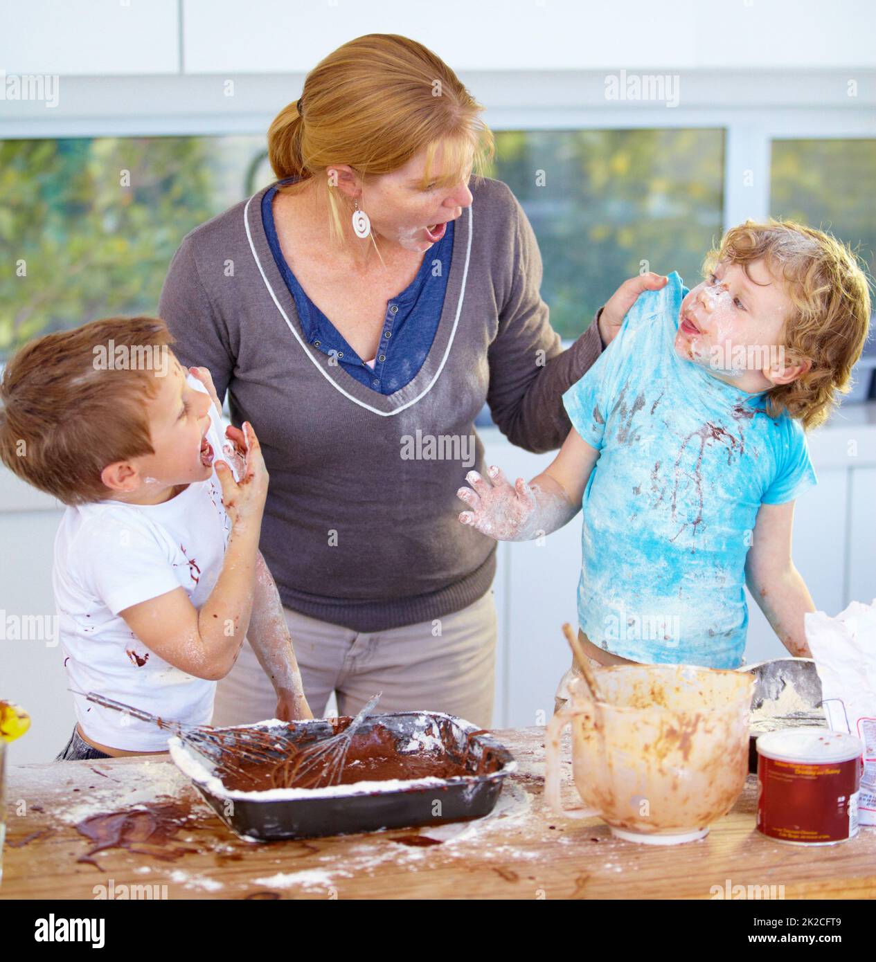Atrapado en el acto. Dos niños que son regañados por su madre por ensuciar su cocina. Foto de stock