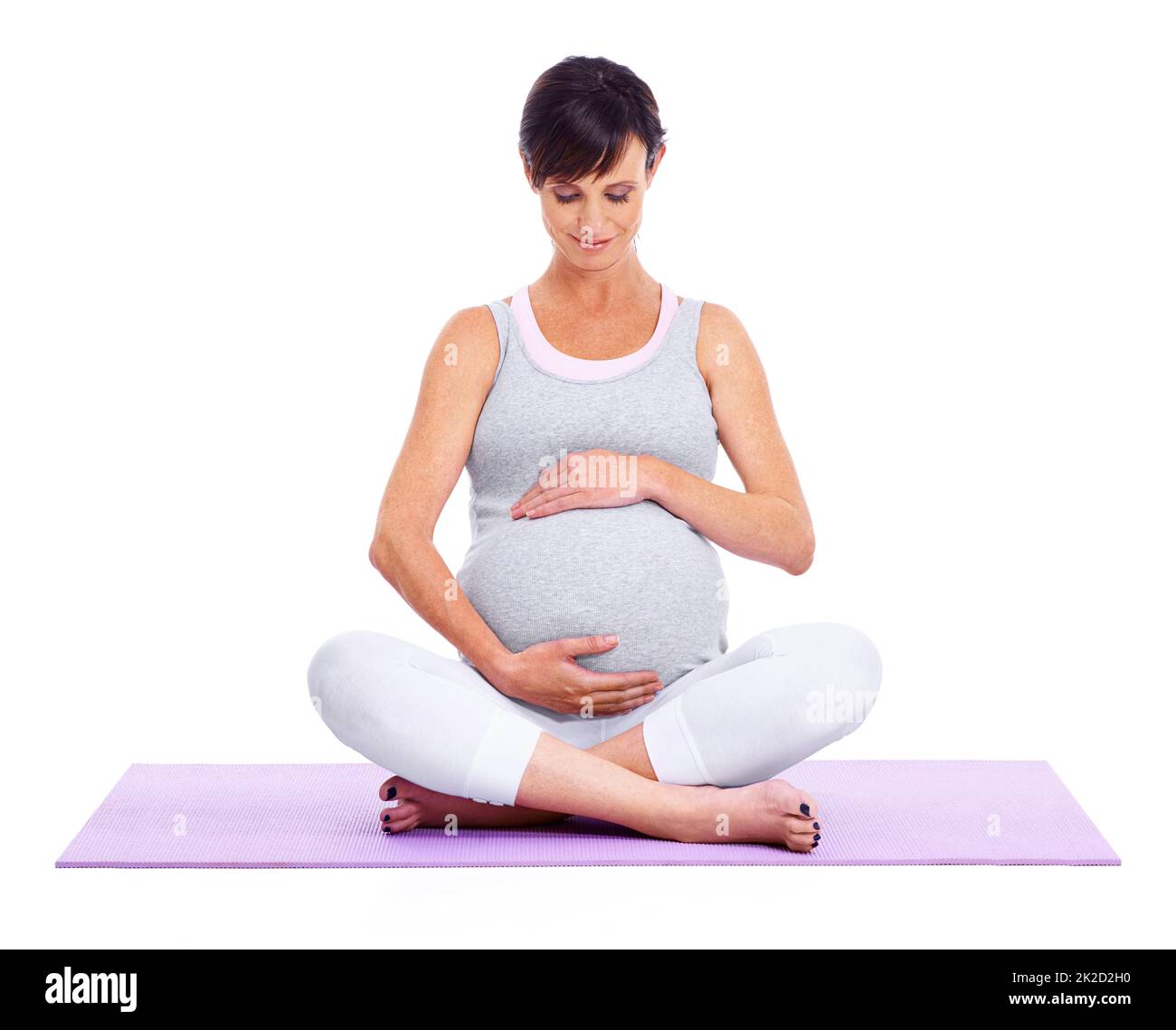 Calma y tranquilidad para mamá y bebé. Una joven madre expectante meditando pacíficamente mientras estaba aislada sobre blanco. Foto de stock