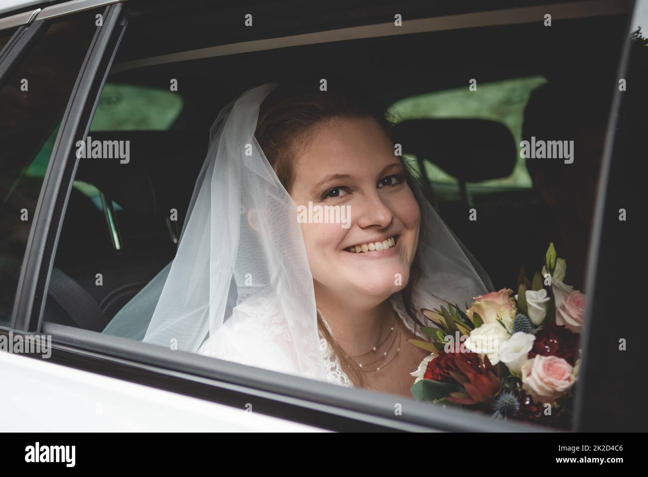 Novia con el pelo marrón sonriendo a la cámara, sentada en un coche Foto de stock