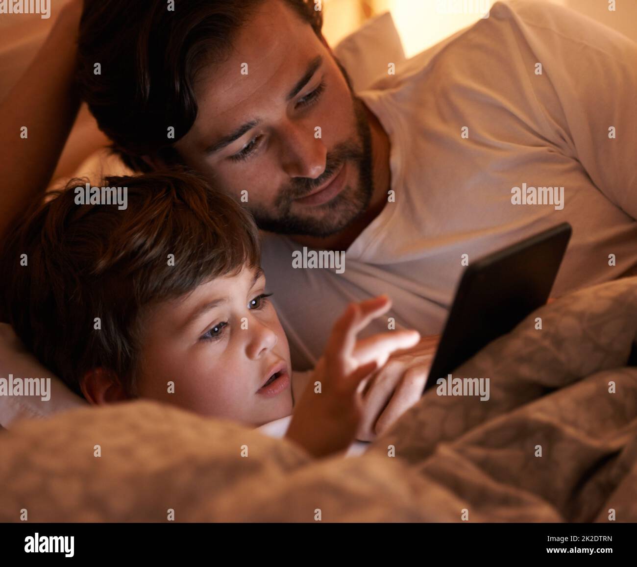 Tiempo de historia digital. Un padre y un hijo acostados en la cama con un lector electrónico. Foto de stock