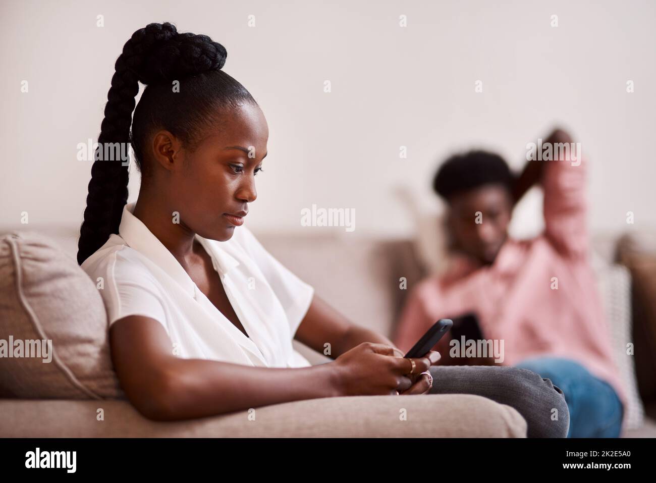 Me llamó un poco de atención en línea. Desenfoque de una mujer usando su celular mientras su pareja se sienta en el fondo. Foto de stock