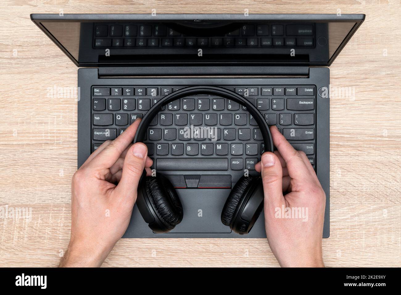Un hombre de negocios sostiene sus modernos auriculares inalámbricos sobre el teclado del portátil Foto de stock