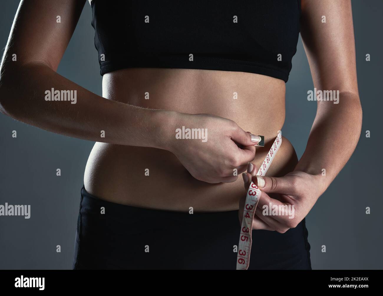 Hazlo por el cuerpo que siempre has querido. Foto recortada de una joven deportiva que mide su cintura. Foto de stock