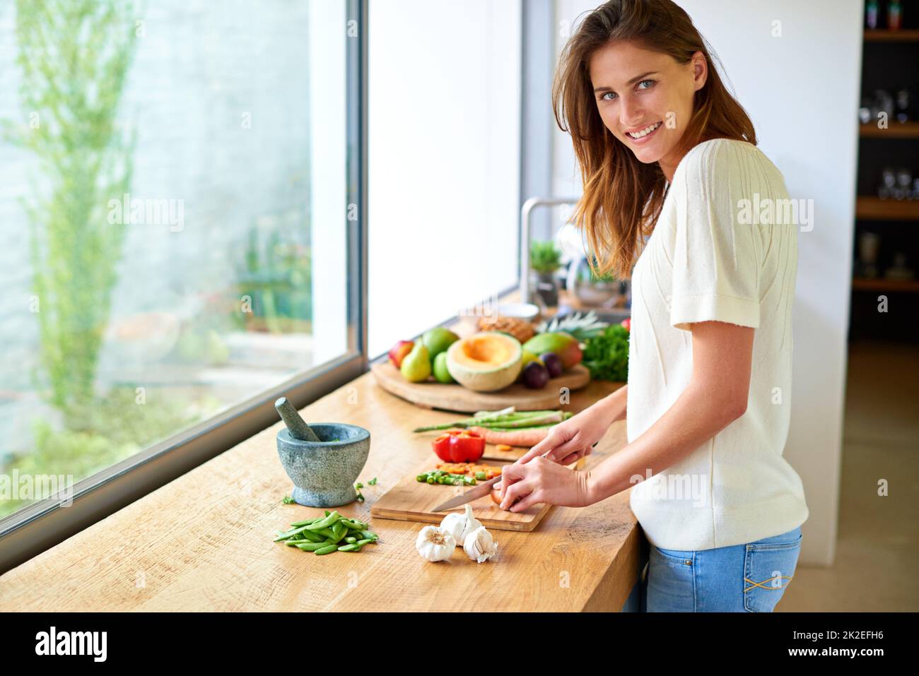Cocinar es mi felicidad. Tiro de una joven atractiva que pica verduras en una cocina. Foto de stock
