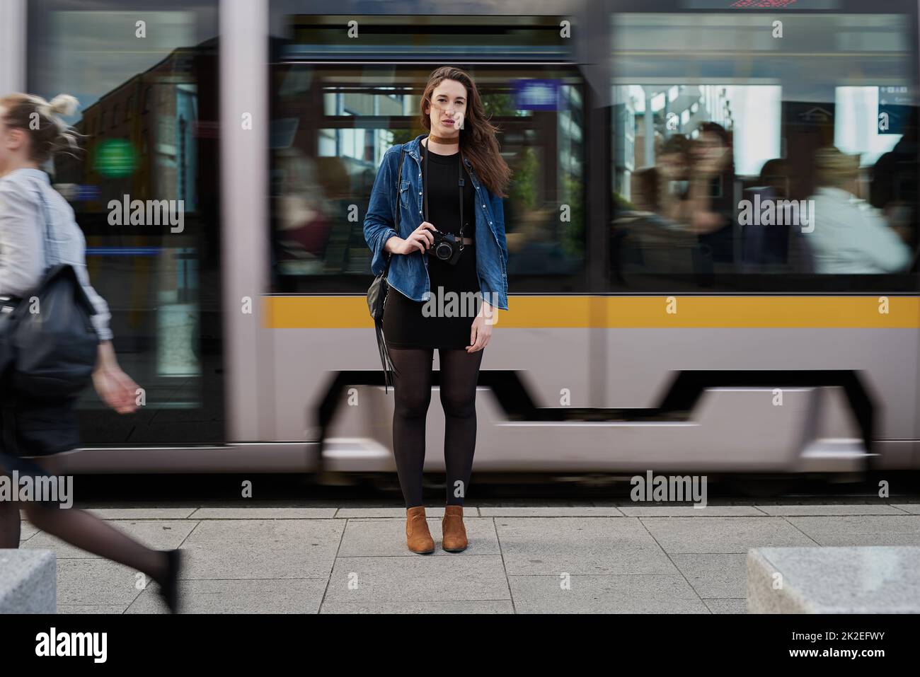 He llegado. Retrato de una joven fotógrafa atractiva parada en el metro con un tren que pasa por el fondo. Foto de stock