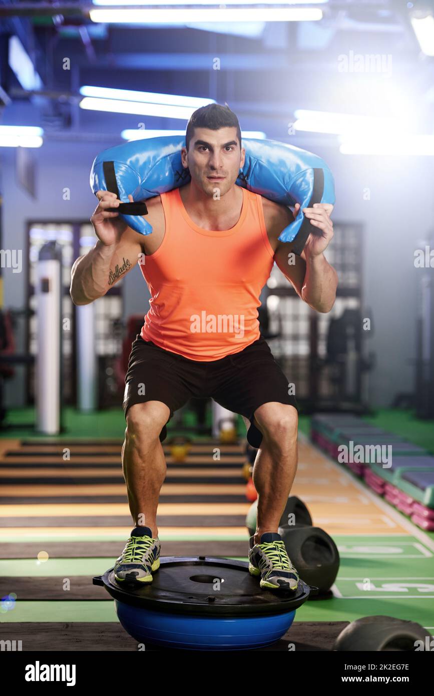 Foto de un joven haciendo ejercicio con una bolsa de arena en el gimnasio. Foto de stock