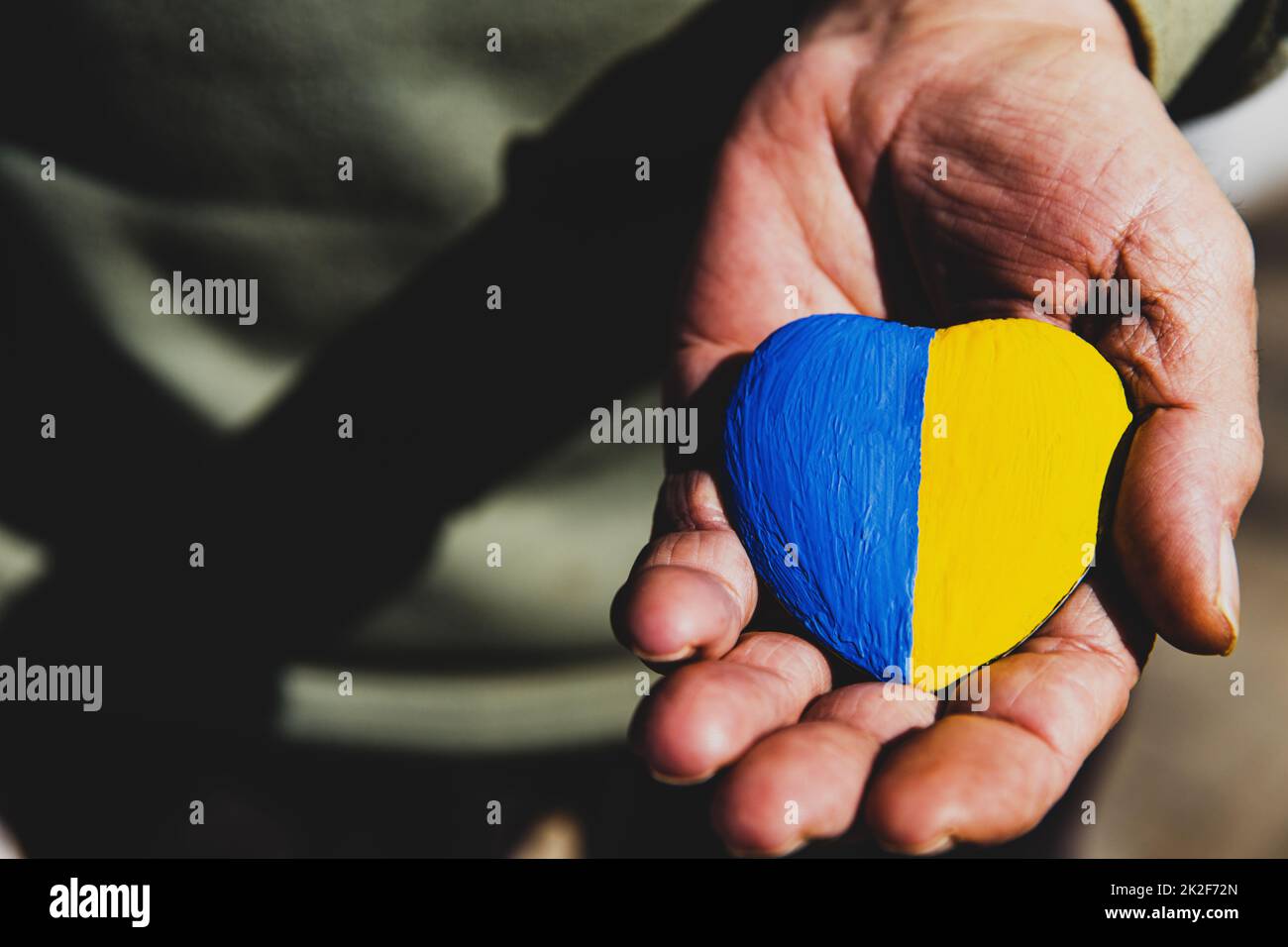 Manos de un hombre mayor o soldado sosteniendo piedra en forma de corazón pintada con la bandera de Ucrania Foto de stock