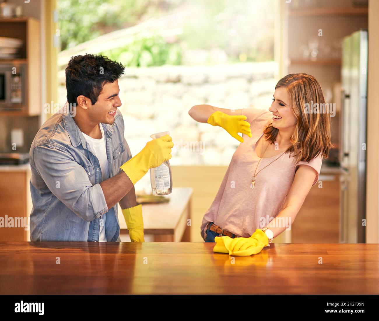 Añadir un poco de diversión a sus tareas domésticas. Una foto de una pareja joven que se desandeaba mientras limpiaba la cocina. Foto de stock