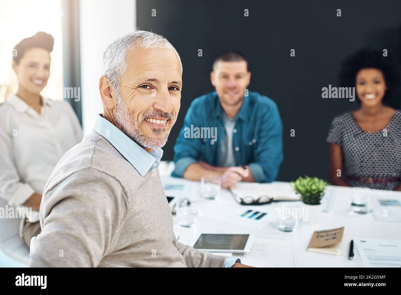 Retrato de un hombre de negocios maduro sentado en una reunión con sus colegas en el fondo. Foto de stock