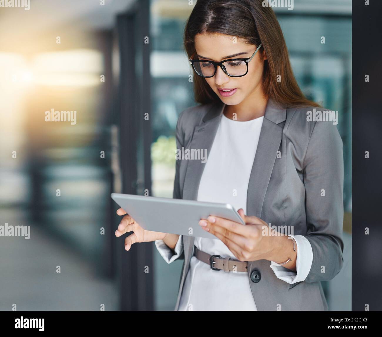 Conectado a la palabra de negocio corporativo. Foto recortada de una joven empresaria atractiva usando su tableta en la oficina. Foto de stock