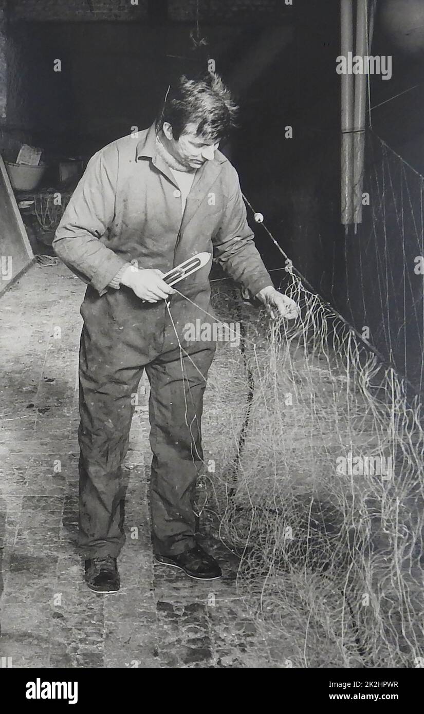 1986 - Un pescador británico haciendo redes de pesca a mano utilizando un transbordador de red Foto de stock