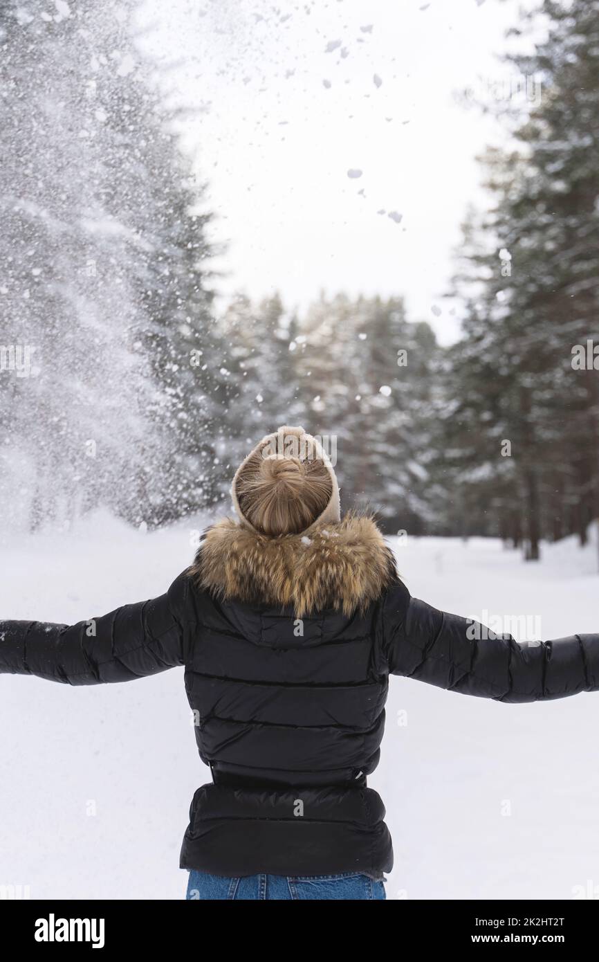 Mujer lanzando nieve al aire durante el frío día de invierno Foto de stock