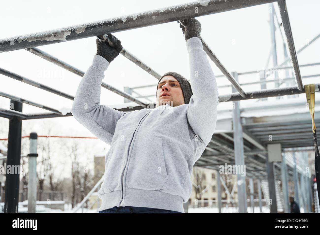 Hombre atlético haciendo pull-ups en la barra horizontal durante su entrenamiento de invierno al aire libre Foto de stock