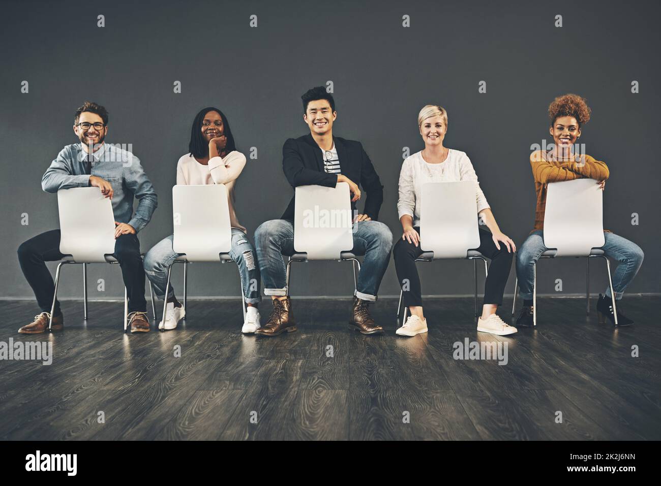 La fila del éxito. Estudio de un grupo diverso de empleados creativos sentados en las sillas del interior. Foto de stock