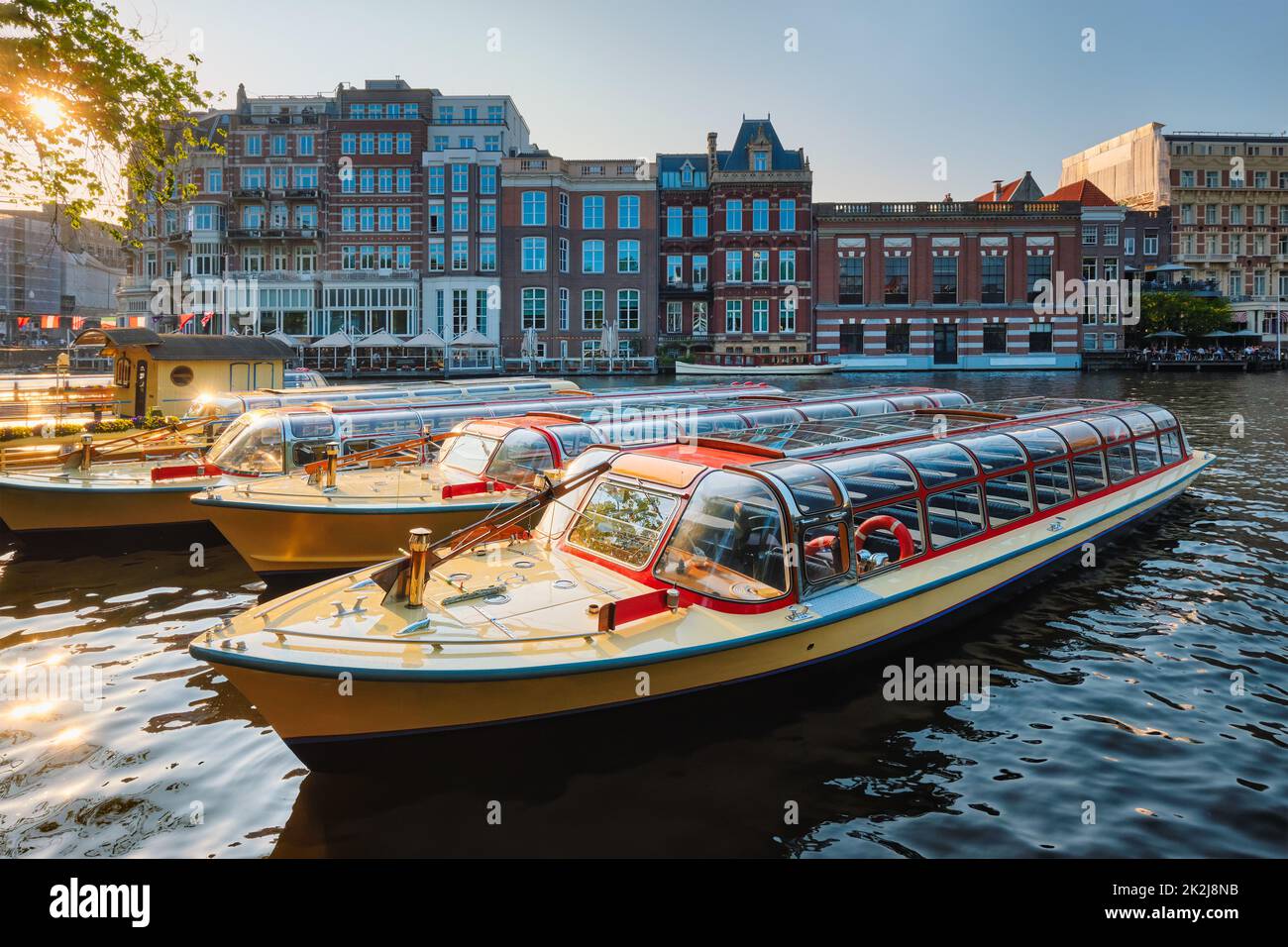 Barcos turísticos amarrados en el muelle del canal de Ámsterdam al atardecer Foto de stock