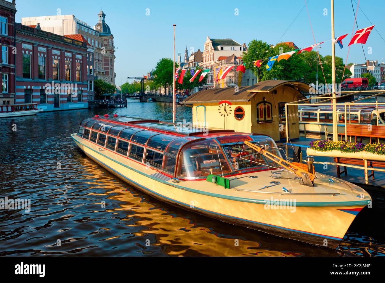 Barcos turísticos amarrados en el muelle del canal de Ámsterdam al atardecer Foto de stock