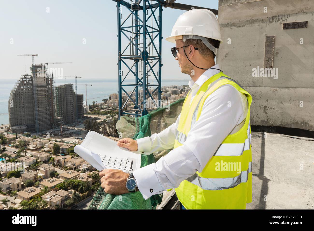 Ingeniero o arquitecto con chaleco reflectante y casco en una obra cerca del mar azul Foto de stock