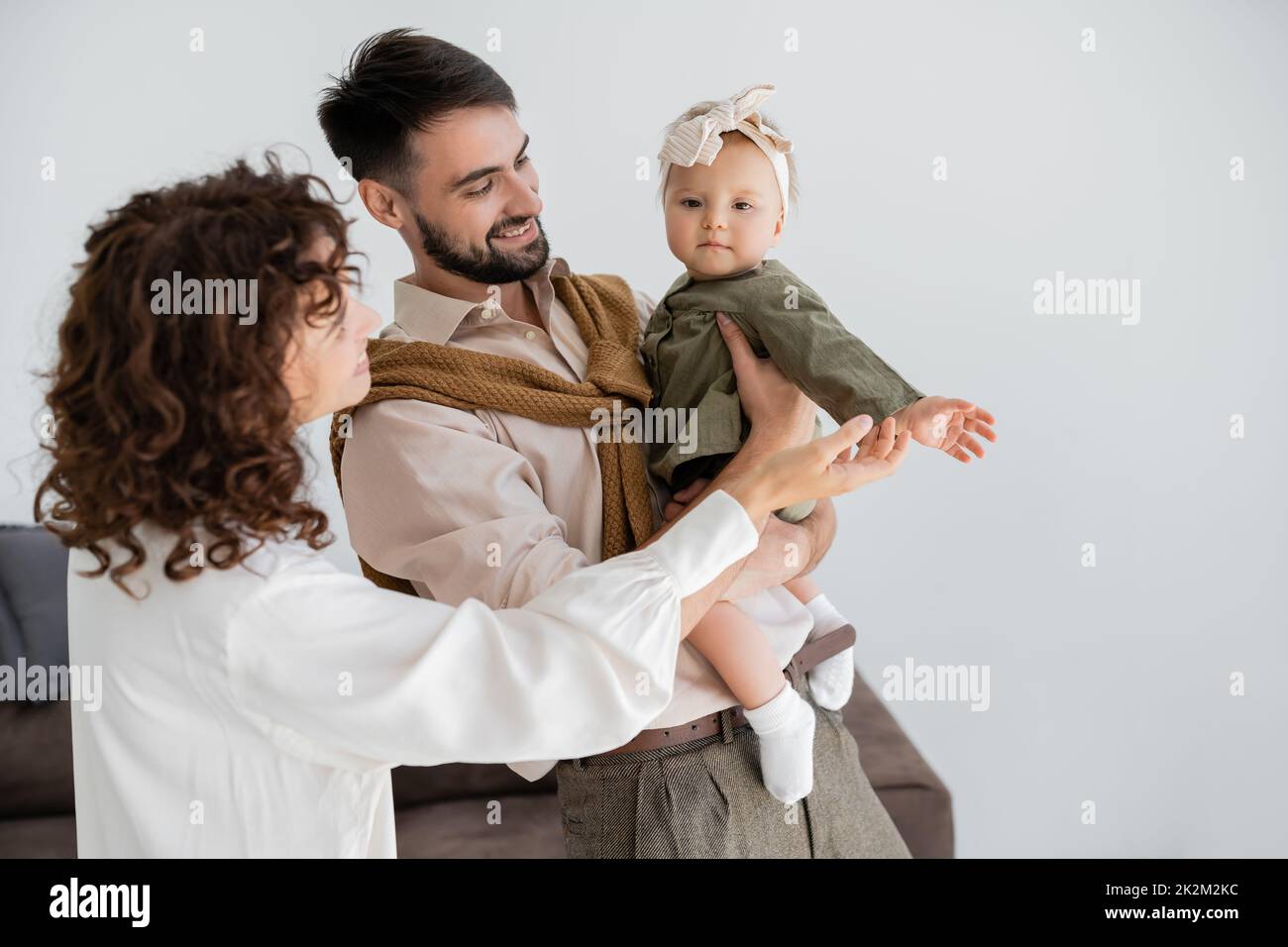 marido satisfecho y esposa rizada que sostiene a bebé muchacha en diadema y vestido, imagen de archivo Foto de stock