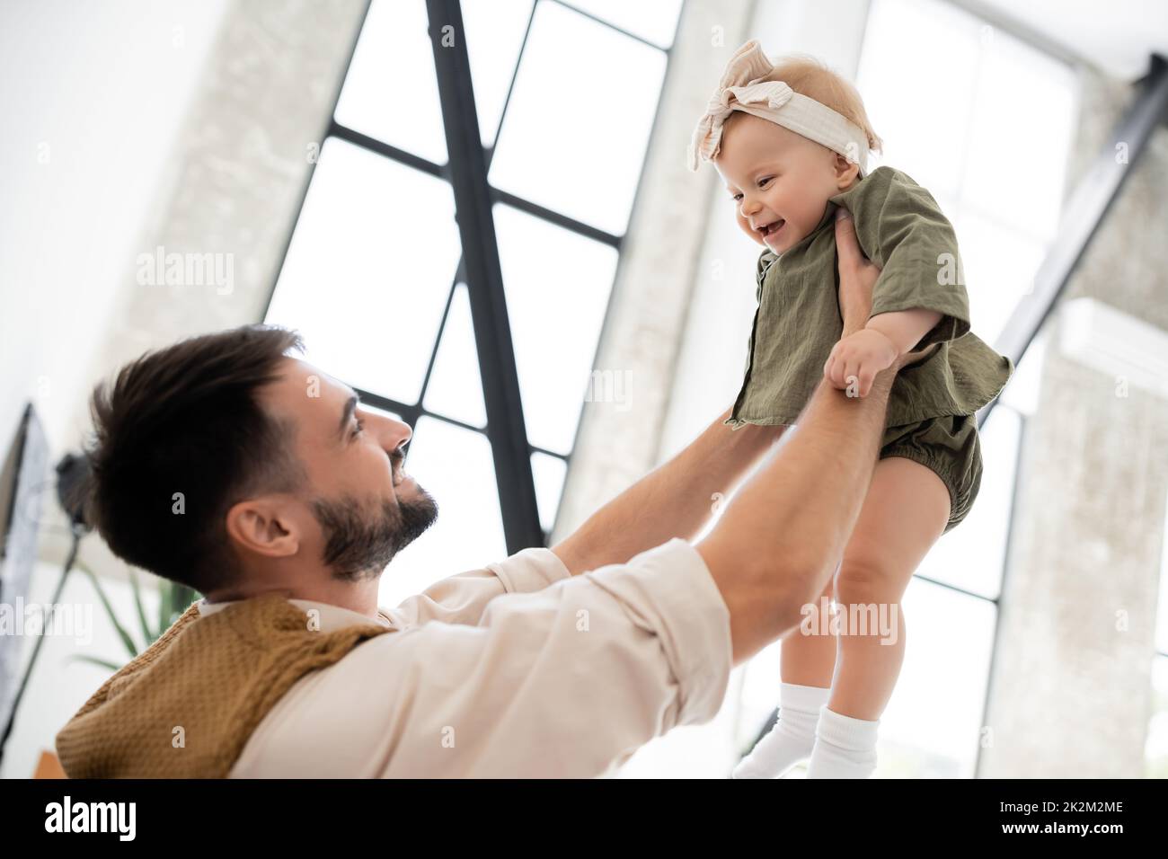 padre alegre sosteniendo a una hija positiva en la diadema y vestido, imagen de archivo Foto de stock