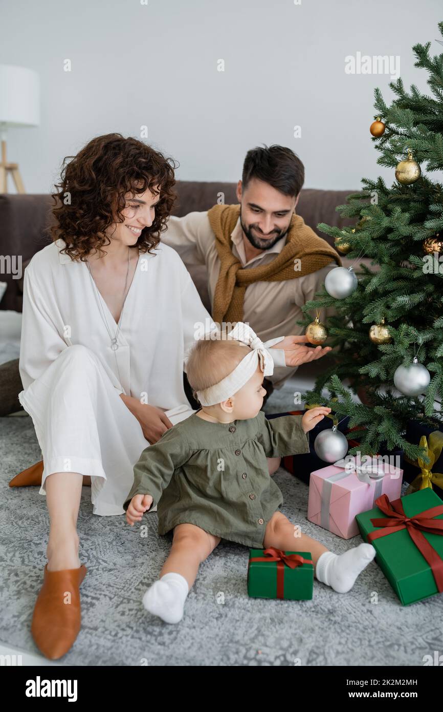 feliz familia con bebé niña sentado cerca del árbol de navidad con regalos, imagen de archivo Foto de stock