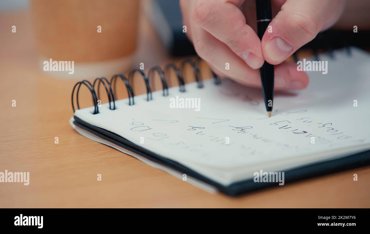 vista recortada de la persona que sostiene el lápiz mientras escribe en un bloc de notas o imagen de archivo borrosa Foto de stock
