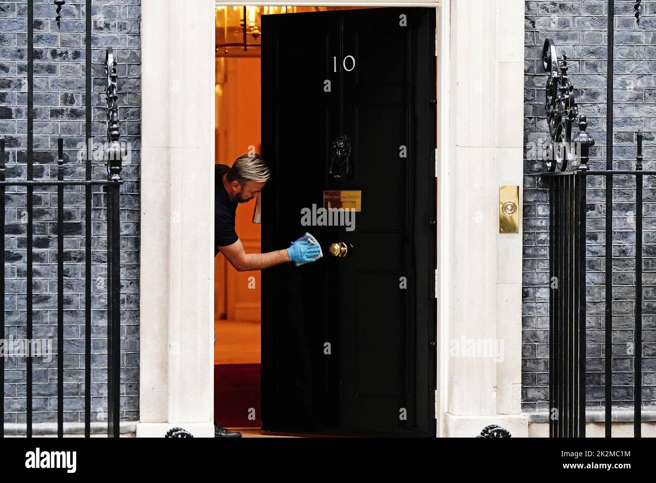 Una persona limpia la puerta principal del 10 Downing Street, Londres. Fecha de la foto: Viernes 23 de septiembre de 2022. Foto de stock