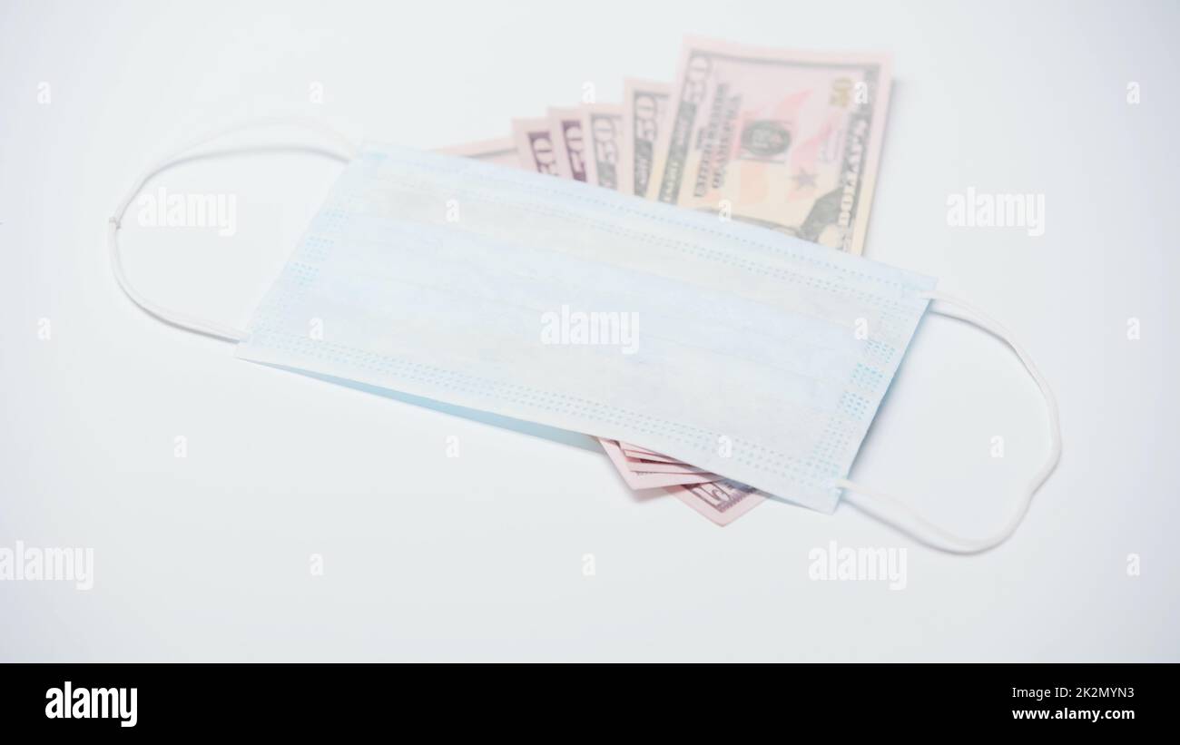 máscara médica protectora en los billetes de dólar sobre fondo blanco Foto de stock