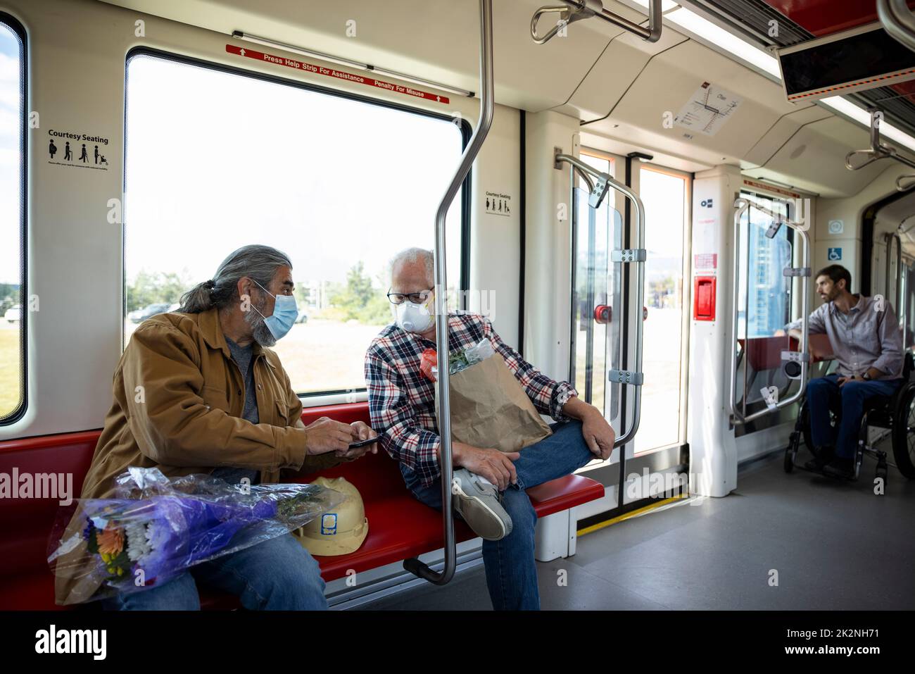 Hombres de edad avanzada con máscaras faciales utilizando un teléfono inteligente en el tren de cercanías Foto de stock