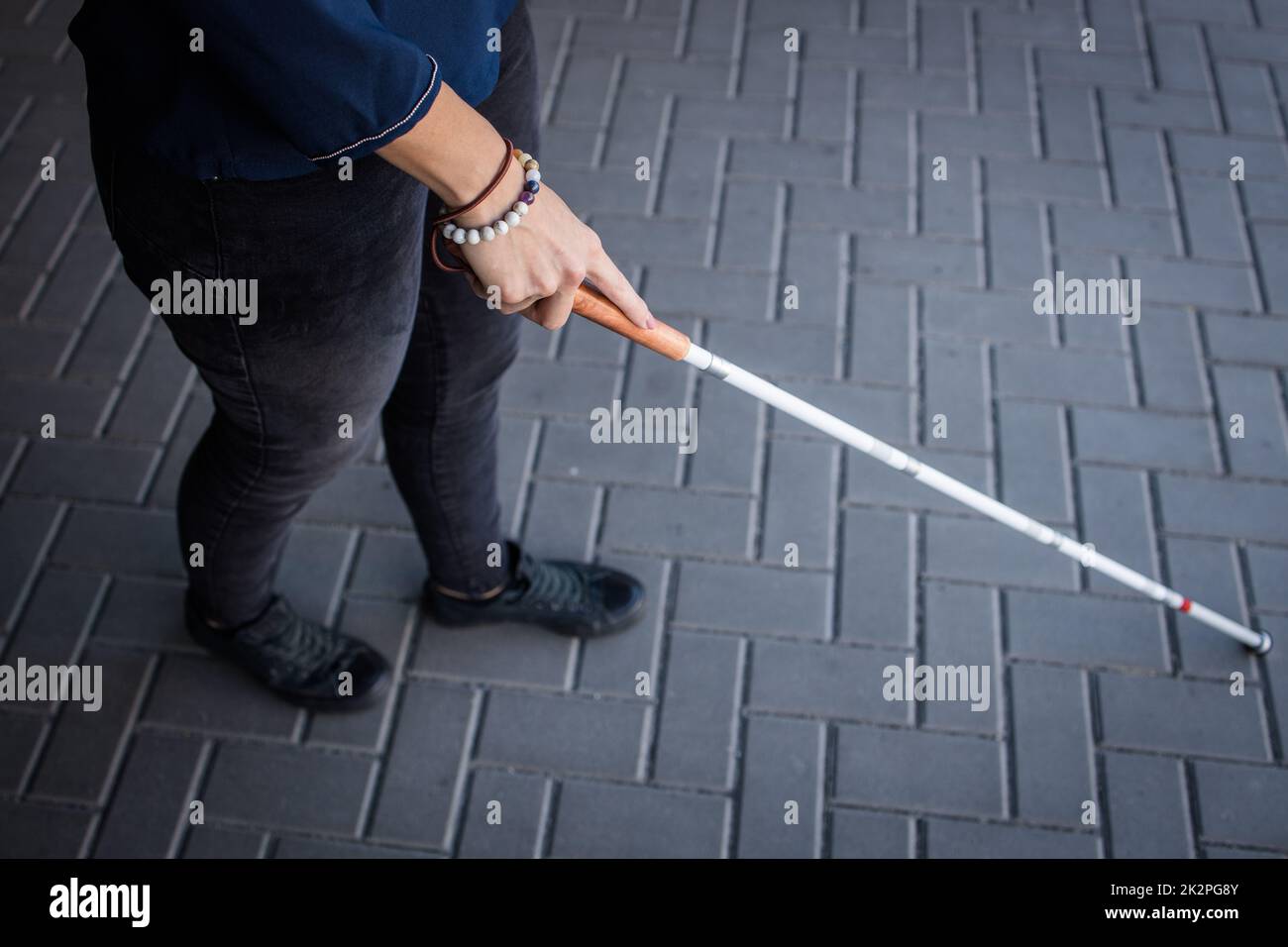 Mujer ciega caminando por las calles de la ciudad, usando su bastón blanco para navegar mejor el espacio urbano y llegar a su destino con seguridad Foto de stock