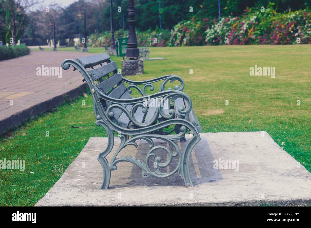 Vista lateral de una silla de jardín, al aire libre al lado de un sendero y campo de césped verde de un parque público en el día soleado durante la puesta de sol. Fondo de la naturaleza Foto de stock