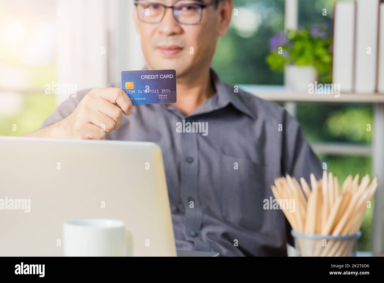 hombre adulto mayor que sostiene una tarjeta de crédito y utiliza la tecnología en el ordenador portátil Foto de stock