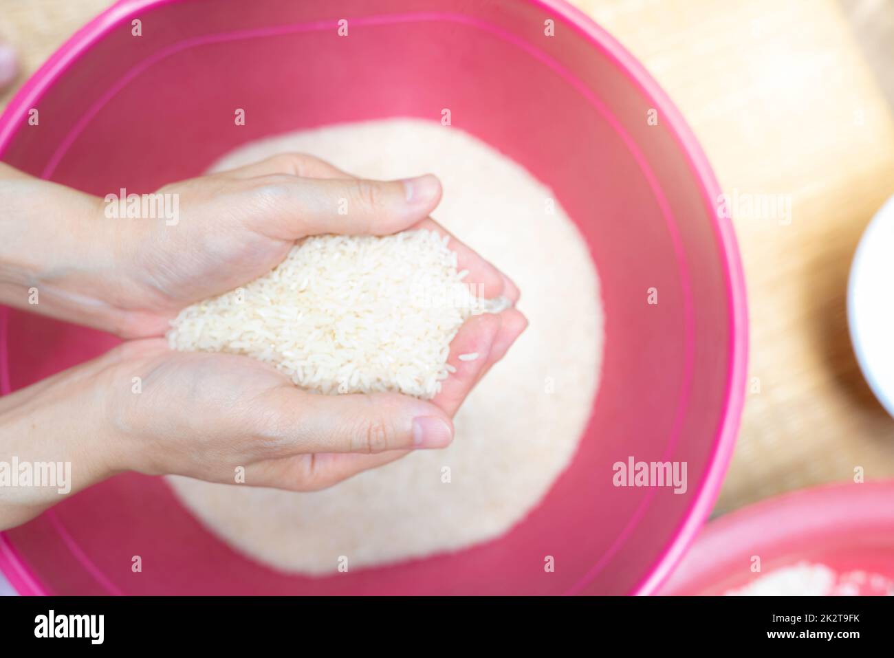 Vista superior de la mano mujer sosteniendo el arroz sobre el tazón de fuente de plástico rojo. Crisis alimentaria mundial. Arroz seco crudo. Arroz blanco blanqueado sin cocinar. Zakat y el concepto de caridad. Cereales orgánicos. El precio del arroz en el mercado mundial. Foto de stock