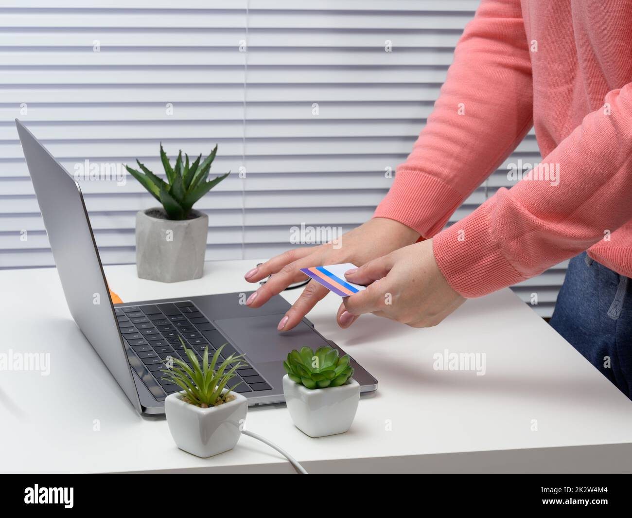 mujer en un suéter rosa hace compras en línea con un ordenador portátil, una tarjeta de crédito en la mano Foto de stock