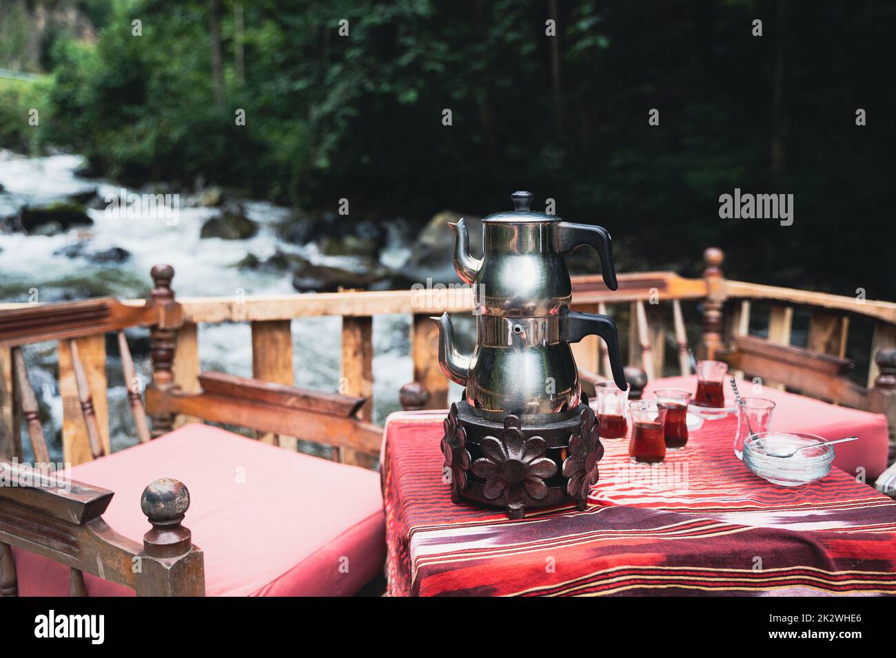 Vista frontal de la tradicional pava turca cromada té y vasos servidos en una mesa de restaurante con sillas cerca de un río en un ambiente al aire libre Foto de stock