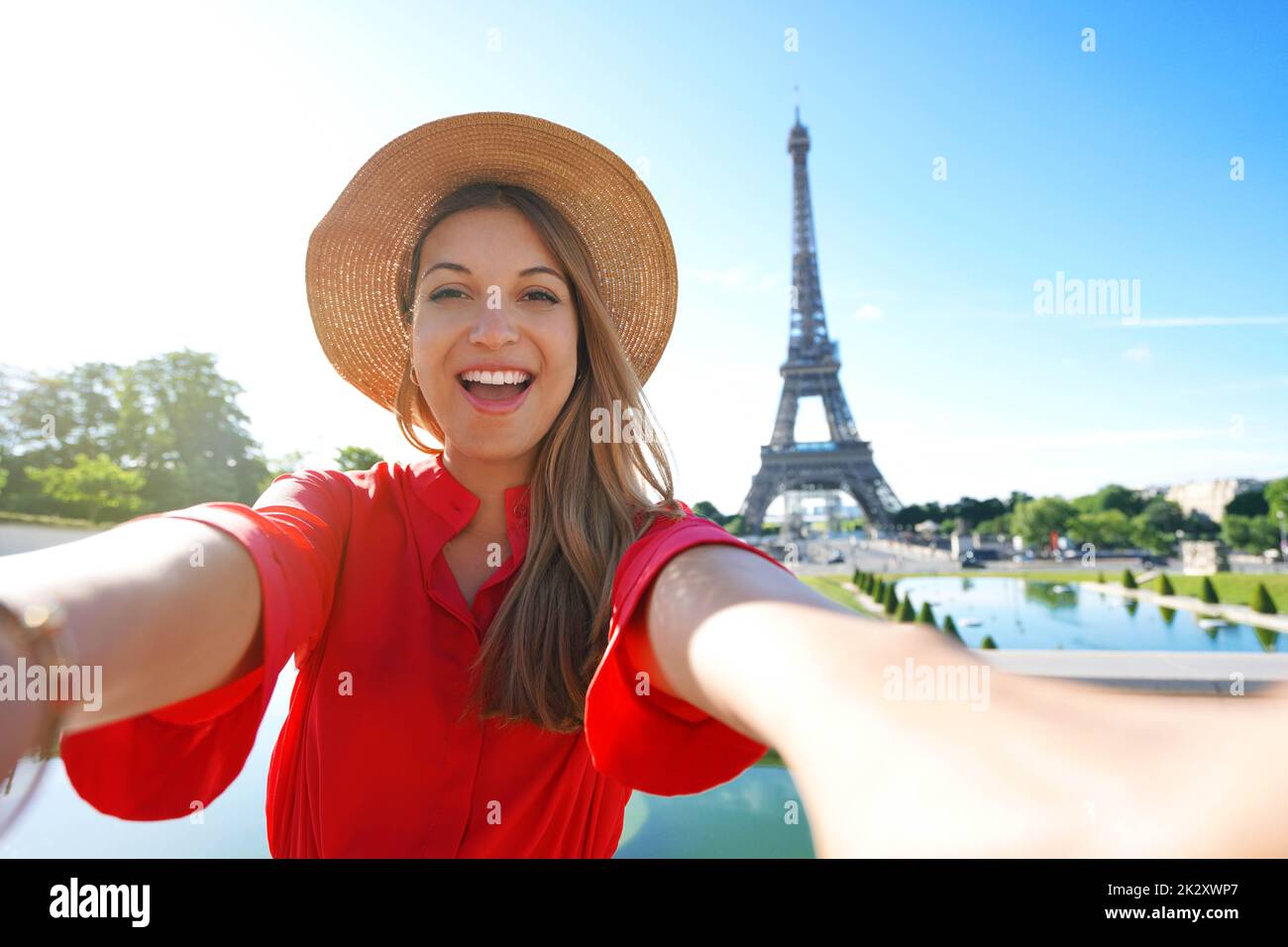 Mujer de moda emocionada con vestido rojo y sombrero se divierte haciendo autorretrato con la Torre Eiffel de fondo en París, Francia. Foto de stock