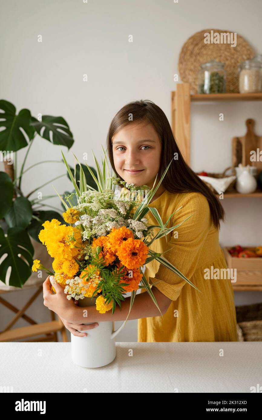 Niña sonriente abrazando jarrón de flores en la mesa de la cocina Foto de stock
