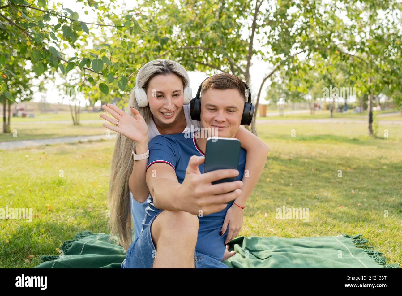 Joven en videollamada a través de un teléfono inteligente con su novia agitando por detrás Foto de stock
