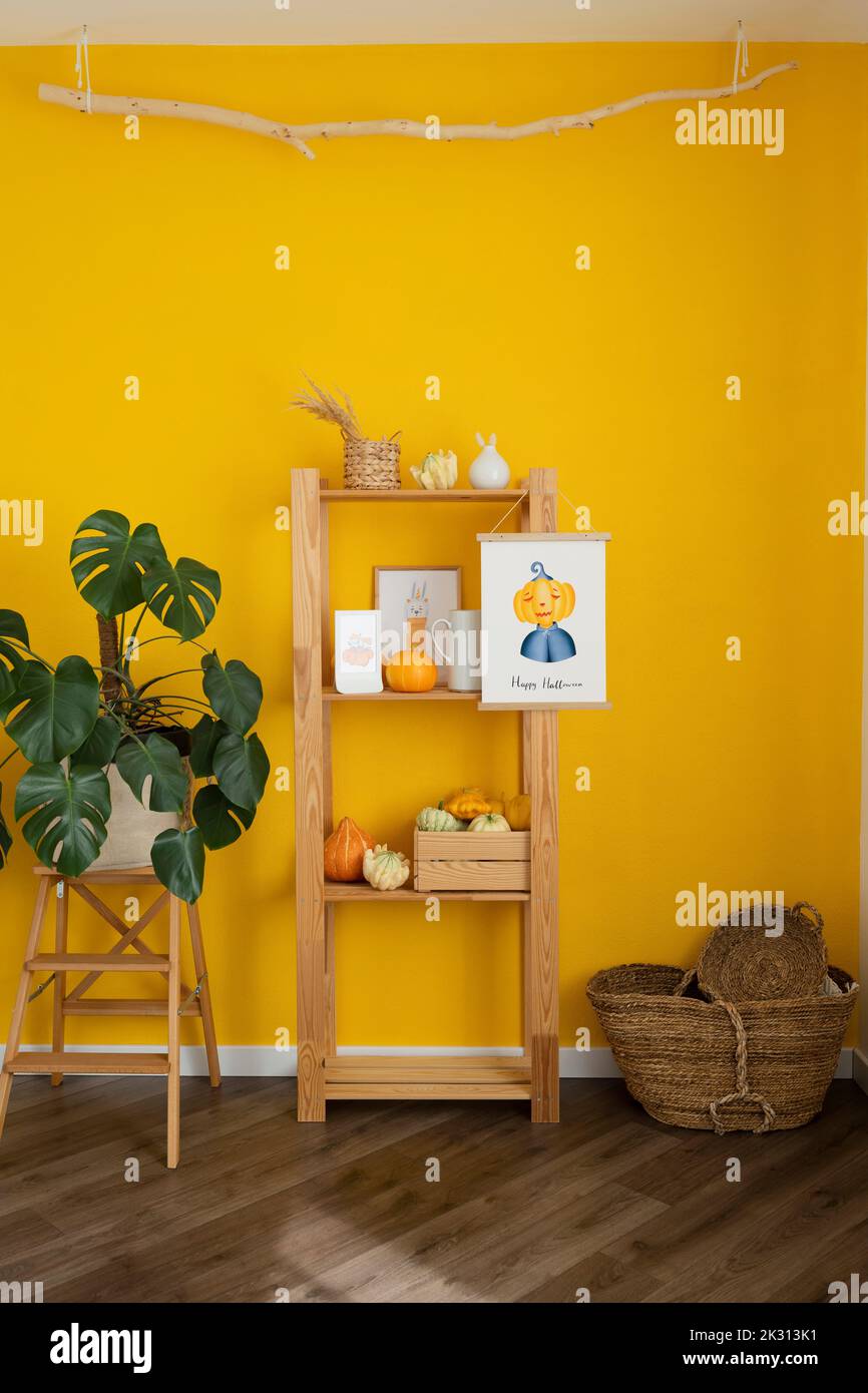Estante de madera con decoración en medio de plantas en macetas y cesta frente a la pared amarilla Foto de stock