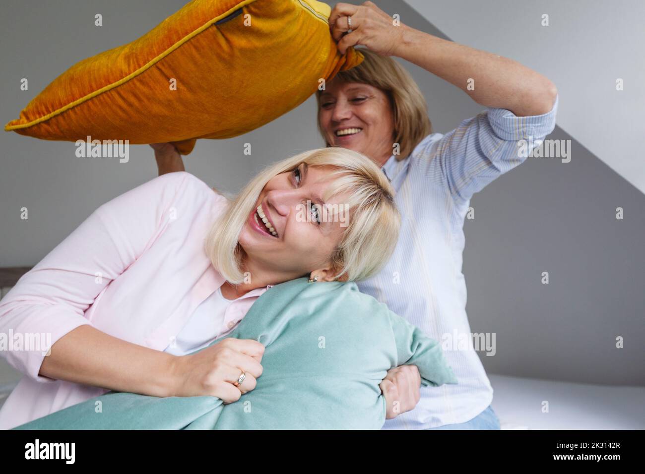 Madre alegre e hija jugando con almohada en la cama en casa Foto de stock