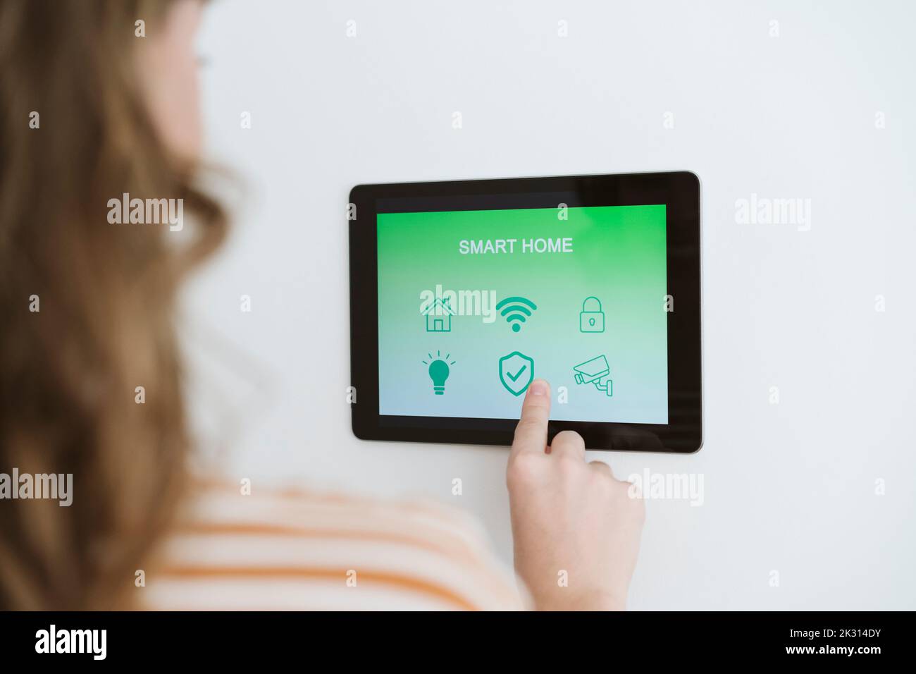 Primer plano de una mujer usando una tableta digital con la aplicación Smart Home en la pared Foto de stock