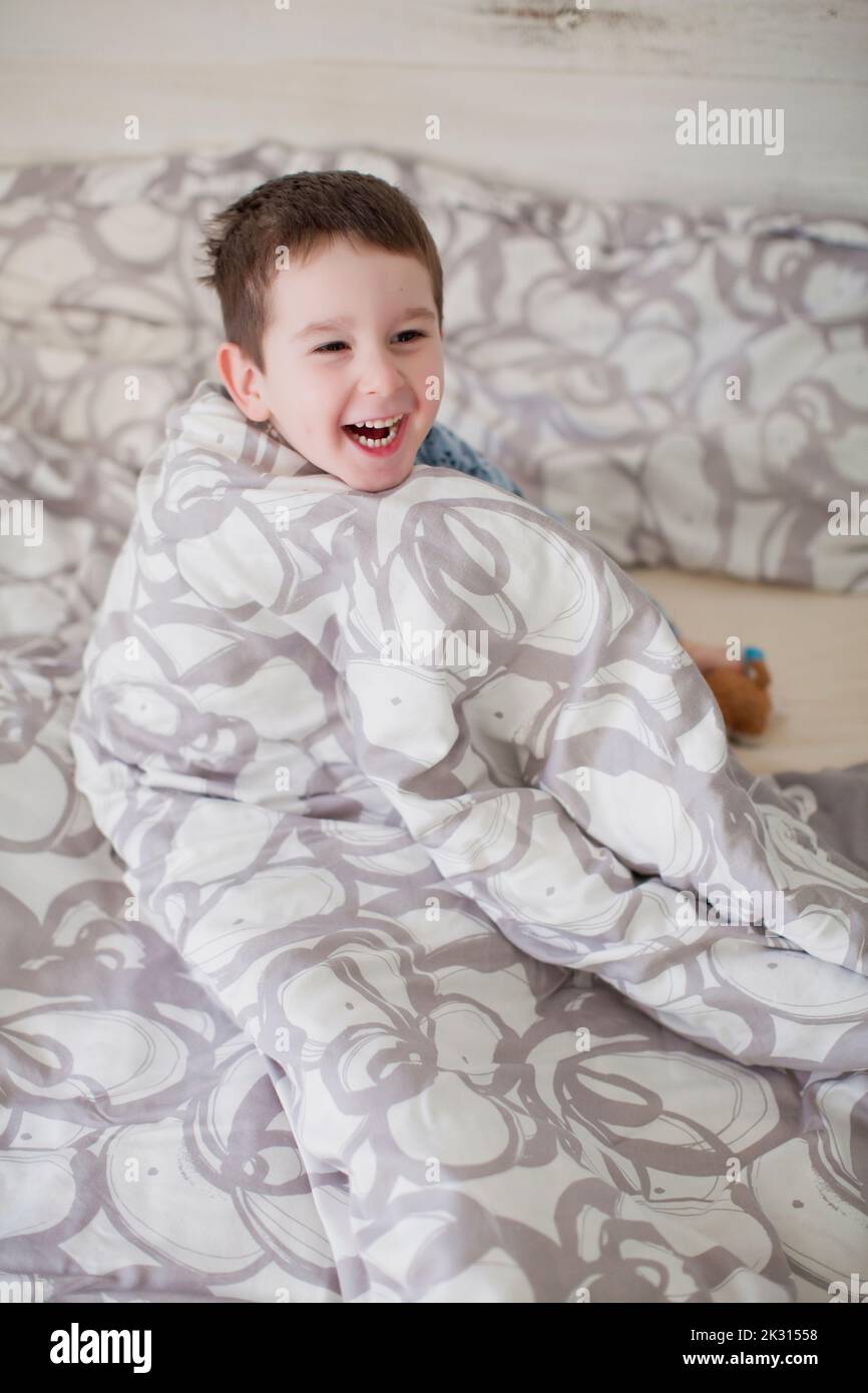 Niño feliz envuelto en una manta en la cama Foto de stock