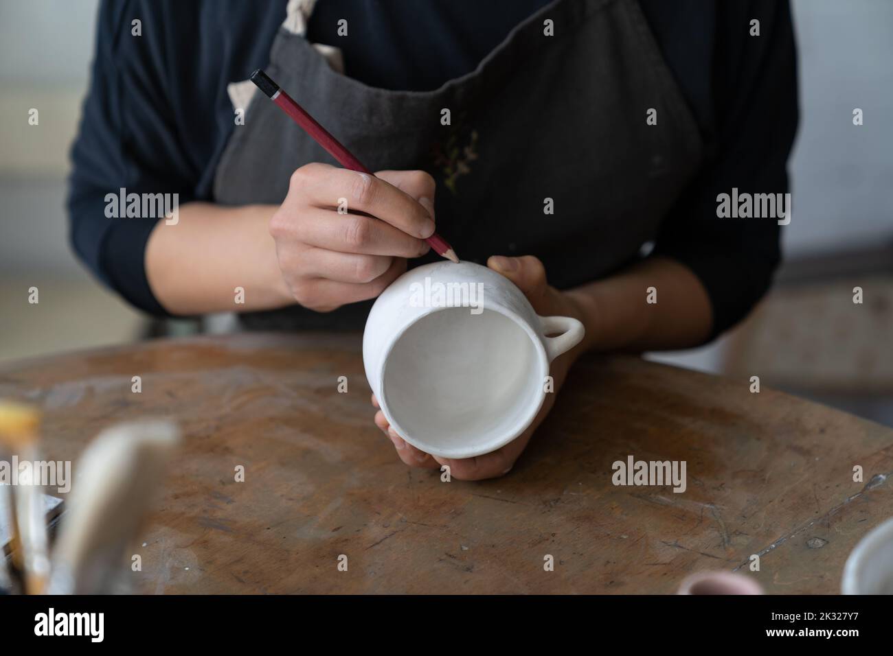 Artesana hace un dibujo del futuro patrón en taza blanca para decorar la cocina con plato de arcilla Foto de stock