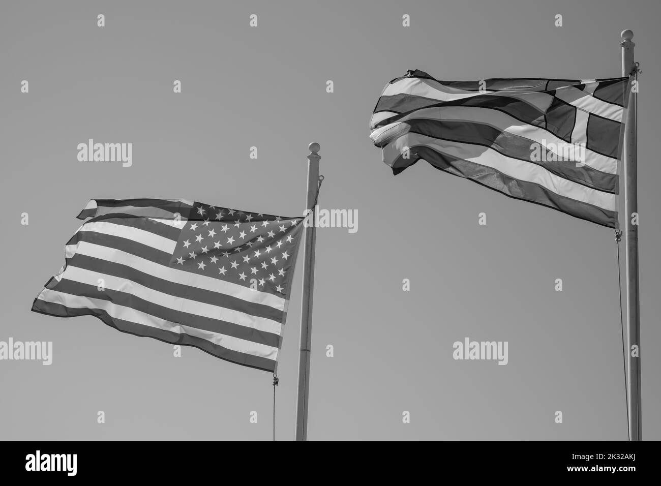 Las banderas nacionales de los Estados Unidos de América y Grecia agitando en el viento y un cielo azul en el fondo en blanco y negro Foto de stock