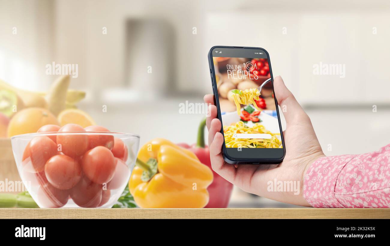 Mujer preparando una comida en su cocina, está buscando recetas saludables en una aplicación de cocina utilizando su smartphone, POV shot Foto de stock