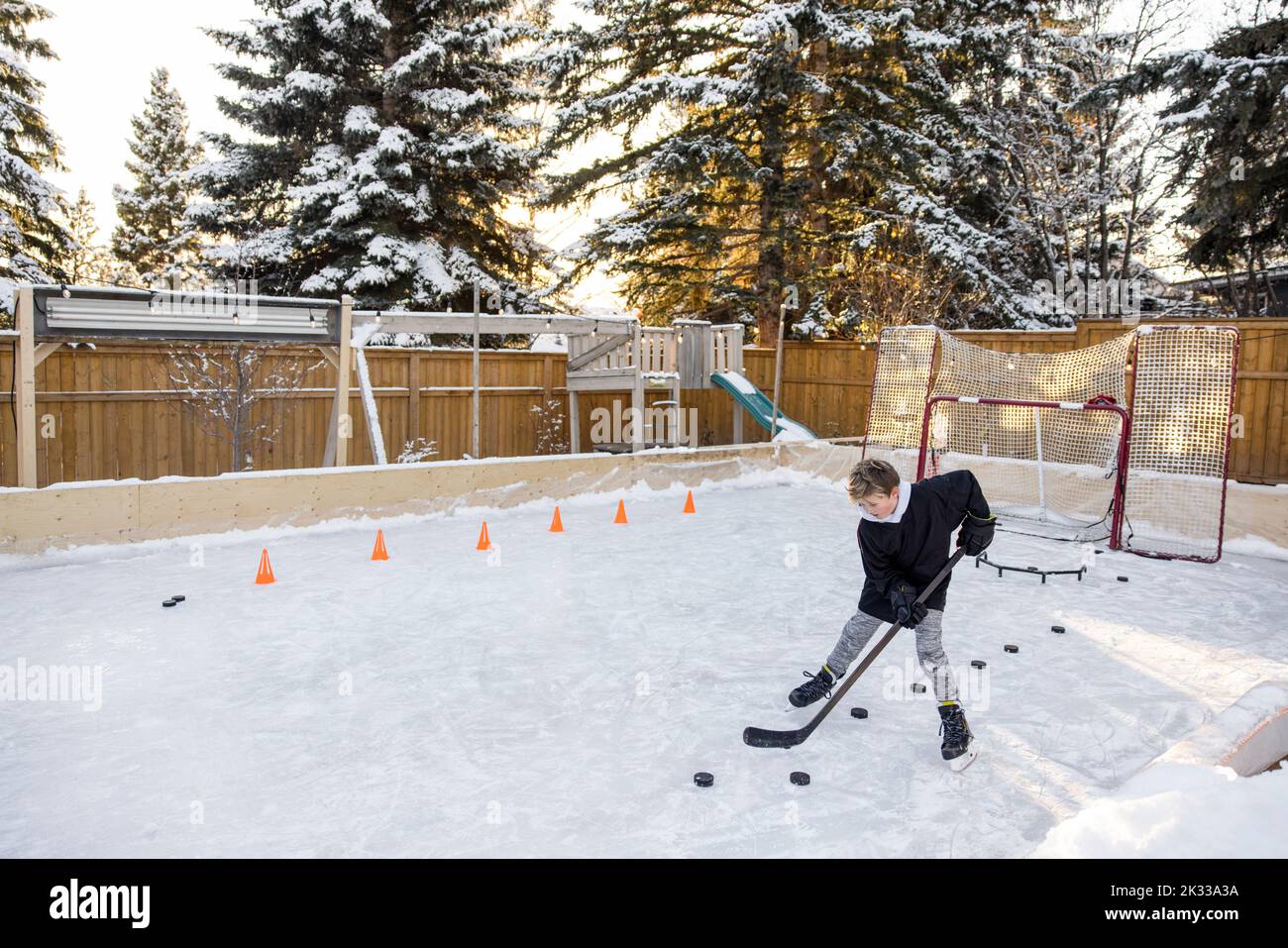 Niño practicando ejercicios de hockey sobre hielo en la pista de patinaje sobre hielo del patio trasero Foto de stock